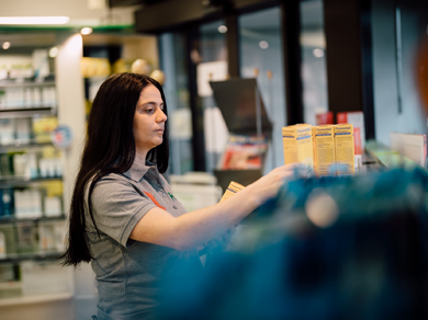 Mitarbeiterin der Medardus Apotheke sortiert Produkte im Verkaufsbereich vor Regalen mit Arzneimitteln.