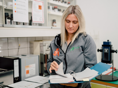 Mitarbeiterin der Medardus Apotheke blättert in einem Ordner im Laborbereich mit Rezeptur-Equipment.